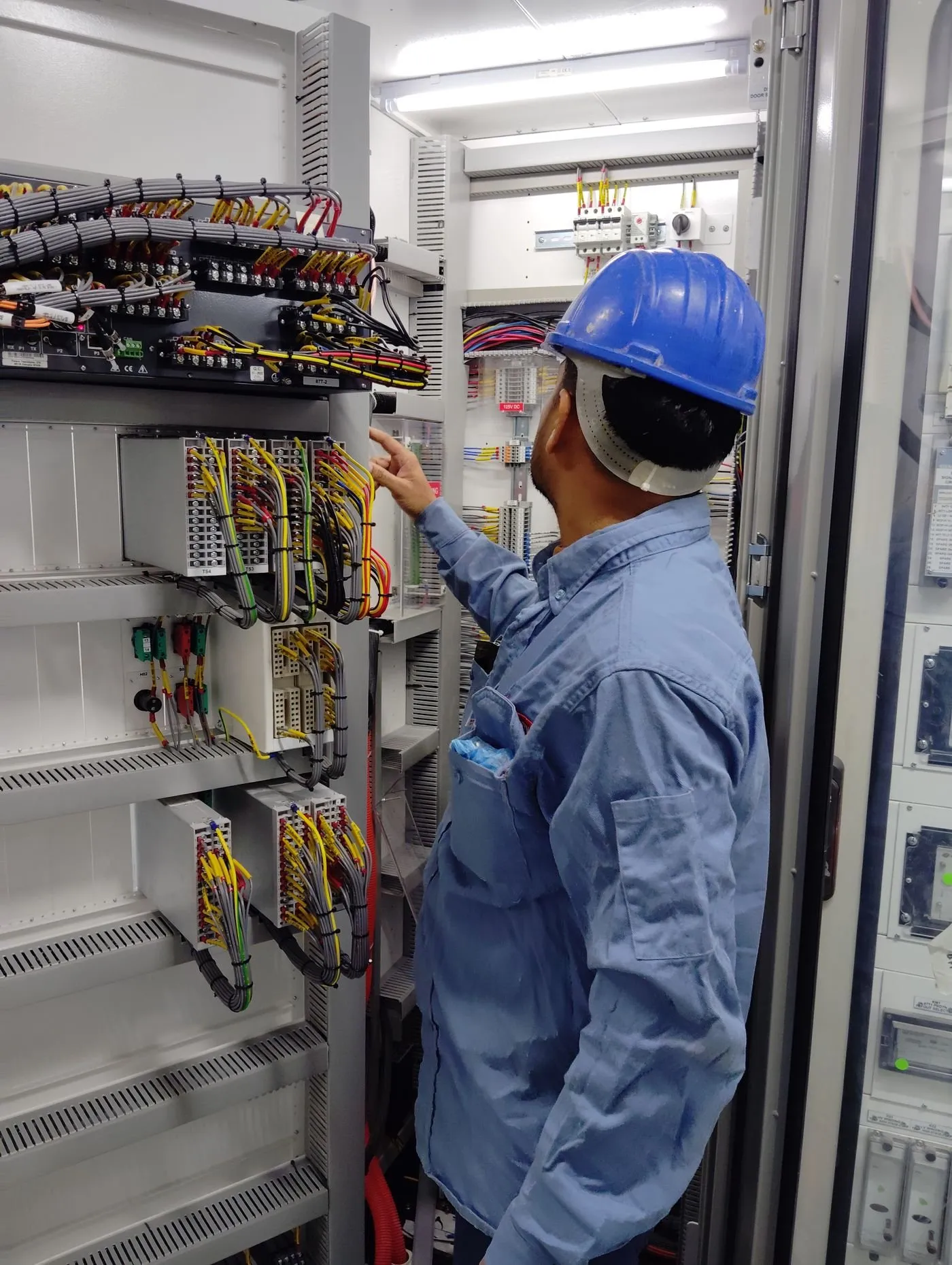 Technician in a safety helmet inspecting an electrical control panel